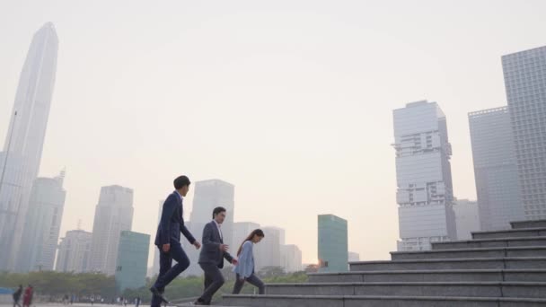 Üç Asyalı şirket yöneticisinden oluşan bir ekip modern şehirde merdivenleri tırmanırken iş konuşuyorlar. - Video, Çekim