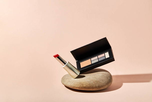 Red lipstick and eyeshadow palette on a river pebble stone with copy space.  - Photo, Image