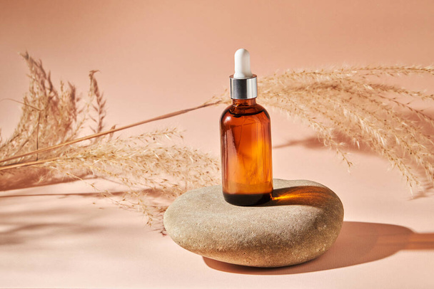 Essential oil on a river pebble stone  on a beige background. Cosmetic medical beauty product in brown glass bottle with a pipette for aromatherapy, alternative medicine. - Foto, Imagem