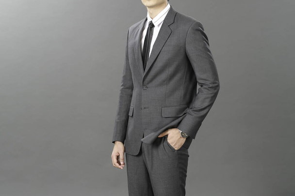 Zakenman draagt een elegant pak over een grijze achtergrond. Goed geklede senior man in de studio die nadenkend denken benadrukt, zorgvuldig nadenkt, zachte focus - Foto, afbeelding