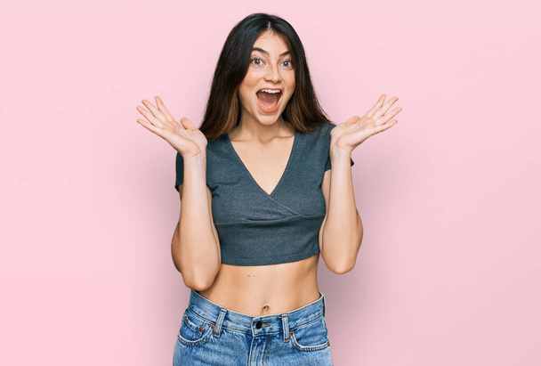 Young beautiful teen girl wearing casual crop top t shirt celebrating crazy and amazed for success with arms raised and open eyes screaming excited. winner concept  - Foto, imagen