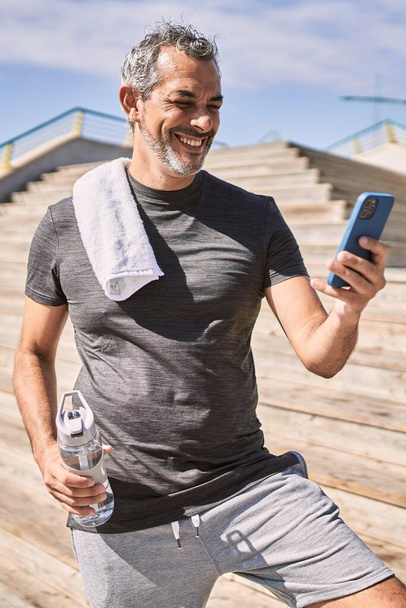 Latynos w średnim wieku, noszący odzież sportową, korzystający ze smartfona na ulicy - Zdjęcie, obraz