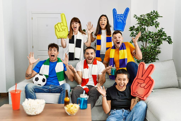 幸せな笑顔で勝利を祝う試合を応援し、手を挙げて勝者の表現を応援する人々のグループ  - 写真・画像