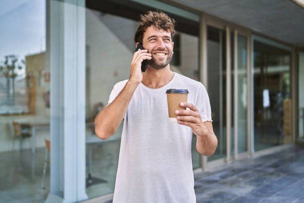 Young hispanic man talking on the smartphone drinking coffee at street - Фото, изображение