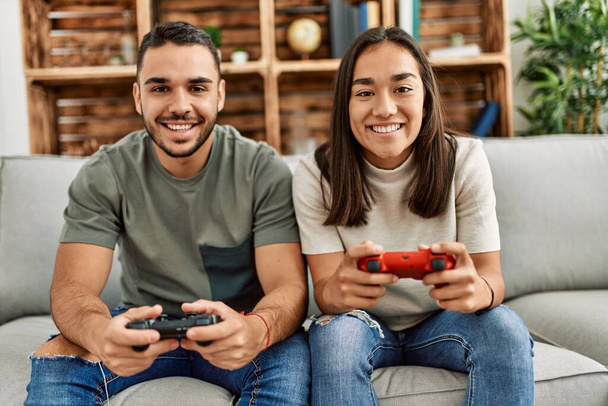 Nuori latino pari hymyilee onnellinen pelaa videopeli kotona. - Valokuva, kuva