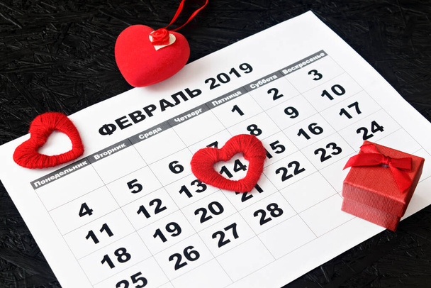 Kalender pagina met rode harten en een geschenk op 14 februari, Valentijnsdag op een zwarte achtergrond. Valentijnskaart. Kalender voor februari in het Russisch. - Foto, afbeelding