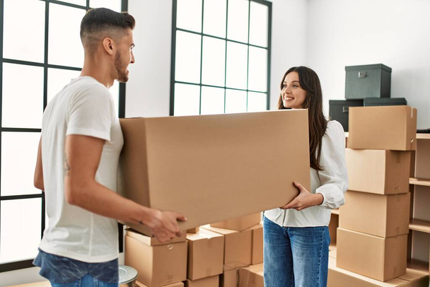 Young hispanic couple smiling happy holding cardboard boxes moving at new home. - Foto, Bild