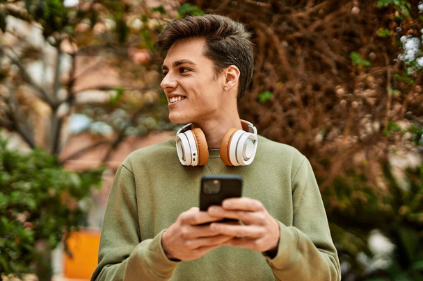Giovane uomo ispanico sorridente felice con smartphone e cuffie in città. - Foto, immagini