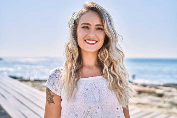 Young blonde girl smiling happy standing at the beach. - Photo, image