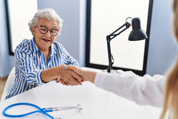 Senior grey-haired woman patient having medical consultation shake hands at clinic - Foto, imagen
