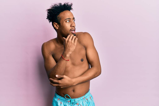 Fiatal afro-amerikai férfi szakállas fürdőruhában stresszesnek és idegesnek tűnik, miközben a kezei körmöket harapdálnak. szorongás.  - Fotó, kép