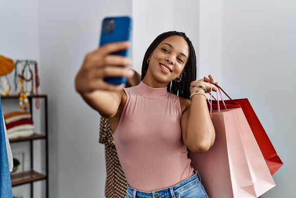 Mladý africký americký žena dělat selfie podle smartphone držení nákupních tašek v obchodě s oblečením - Fotografie, Obrázek