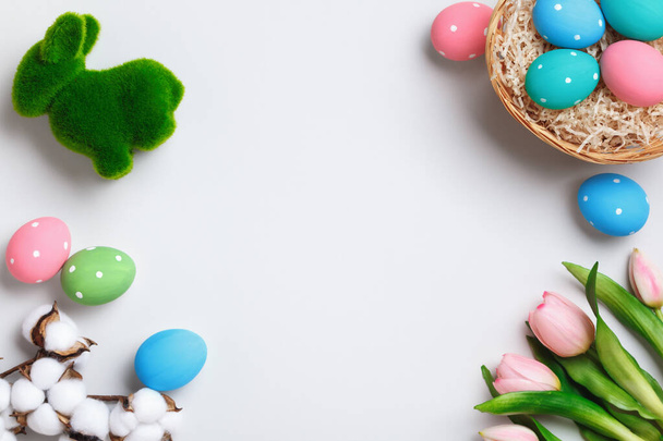 Easter composition. Multi-colored eggs in a basket, tulips rabbit flowers on a gray background. Flat lay top view copy space for greeting cards. - Foto, Imagem