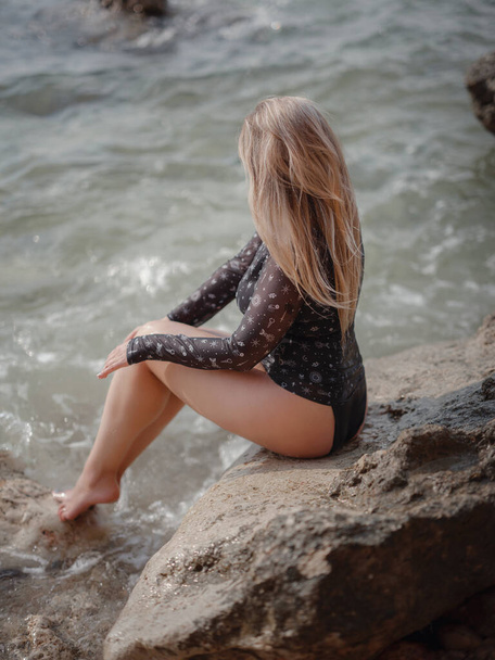 Portret van een aantrekkelijke Amerikaanse blonde vrouw met lang haar poserend op rotsachtig strand. Mooi pluspunt - Foto, afbeelding