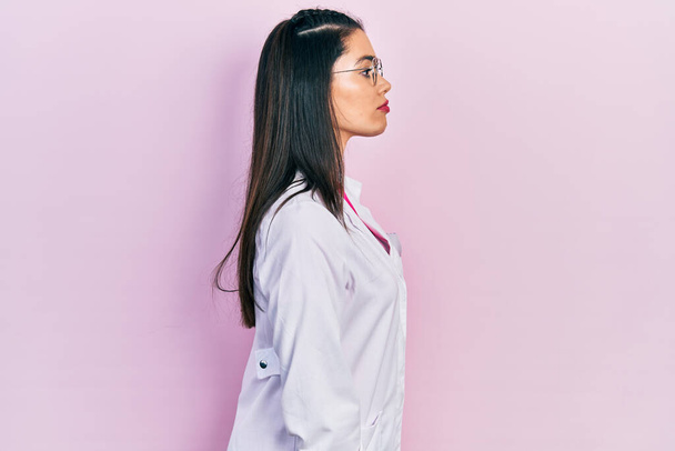 Young hispanic girl wearing scientist uniform looking to side, relax profile pose with natural face with confident smile.  - Photo, Image