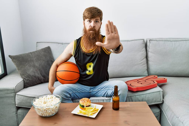 Uzun sakallı, basketbol topu tutan beyaz adam televizyon oyunu tezahüratı yapıyor ve avuç içiyle şarkı söylemeyi kesiyor. Yüzünde olumsuz ve ciddi bir jest olan uyarı ifadesi.  - Fotoğraf, Görsel