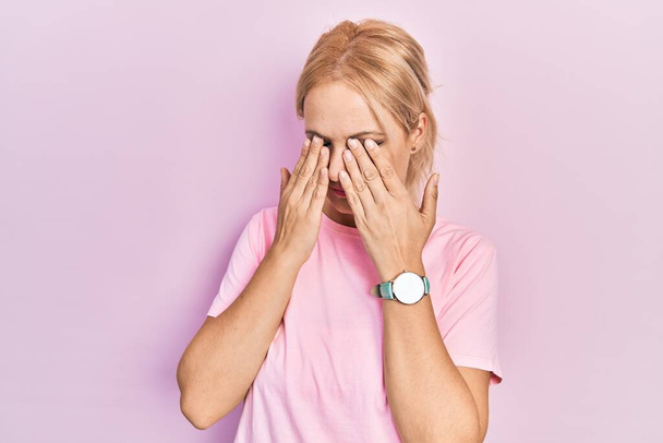 Mladá blondýnka v neformálním růžovém tričku si mnula oči pro únavu a bolest hlavy, ospalý a unavený výraz. problém s viděním  - Fotografie, Obrázek