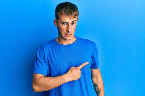 Молодой кавказский мужчина в обычной синей футболке, указывая в сторону взволнованный и нервный указательным пальцем, обеспокоенный и удивленный выражение лица  - Фото, изображение