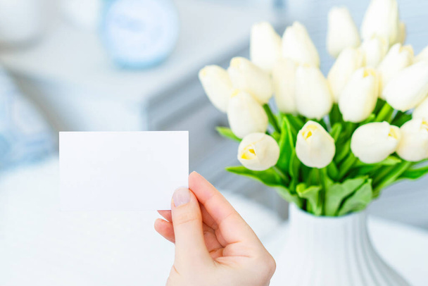 Woman pulling blank greeting card from bouquet of white tulips flowers. Woman day, Copy space. Mock up - Фото, зображення