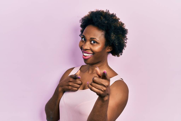 Young african american woman wearing casual sleeveless t shirt pointing fingers to camera with happy and funny face. good energy and vibes.  - Photo, Image