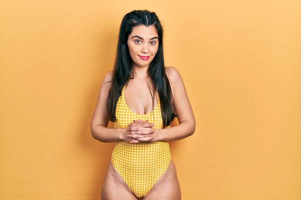 Young hispanic girl wearing swimsuit with hands together and crossed fingers smiling relaxed and cheerful. success and optimistic  - Foto, imagen