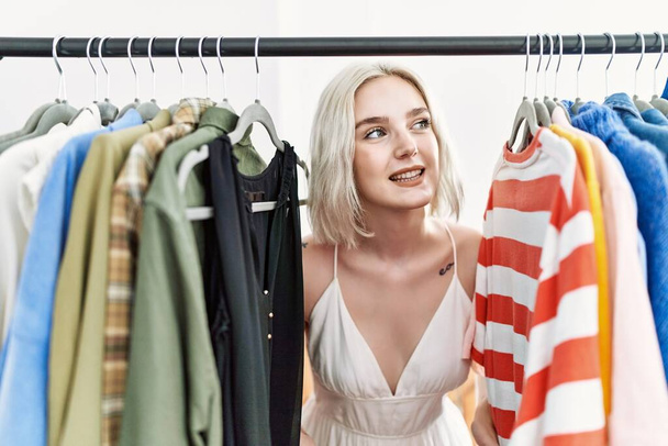Joven mujer caucásica sonriendo confiada apareciendo a través de la ropa en la tienda de ropa - Foto, imagen