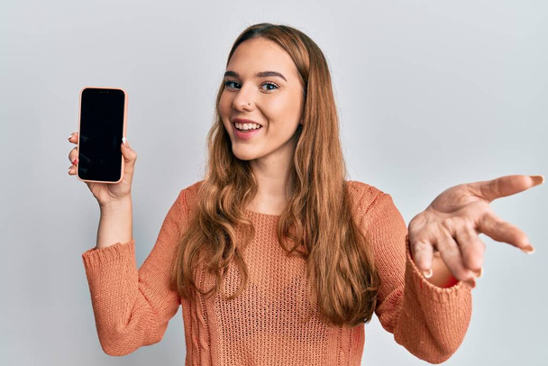 Young blonde woman holding smartphone showing screen celebrating achievement with happy smile and winner expression with raised hand  - Photo, image