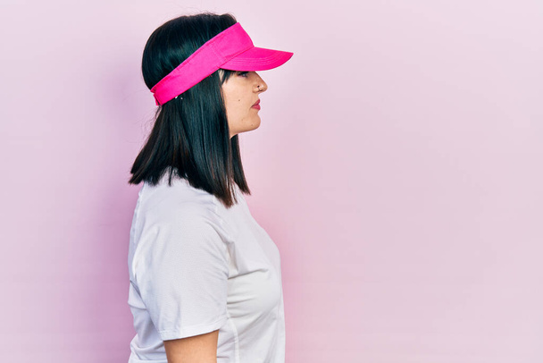 Young hispanic woman wearing sportswear and sun visor cap looking to side, relax profile pose with natural face with confident smile.  - Photo, Image