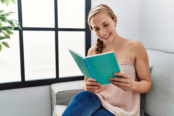 Young caucasian woman reading book sitting on sofa at home - Photo, Image