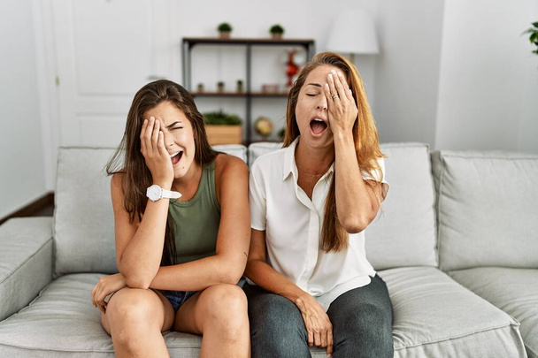 Mother and daughter together sitting on the sofa at home yawning tired covering half face, eye and mouth with hand. face hurts in pain.  - Φωτογραφία, εικόνα