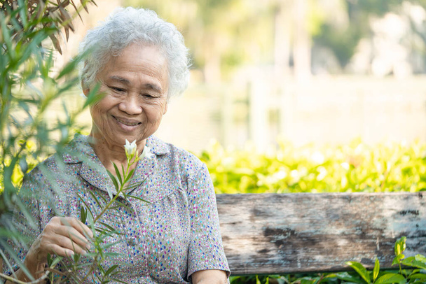 Asiática senior o anciana anciana mujer de edad sosteniendo rosa roja flor, sonrisa y feliz en el jardín soleado. - Foto, imagen