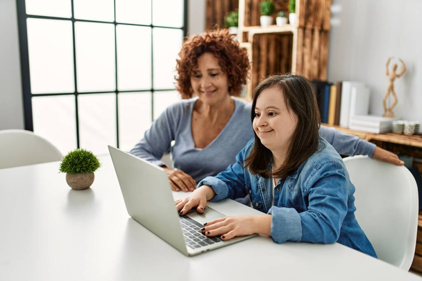 Mature mother and down syndrome daughter using computer laptop at home - Foto, afbeelding