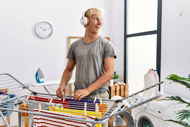 Giovane uomo caucasico ascoltare musica appeso vestiti in lavanderia - Foto, immagini