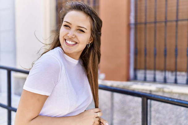 Attraktive und schöne hispanische Frau, die an einem sonnigen Tag im Freien glücklich lächelt. Hübsches brünettes Mädchen mit positivem Lächeln blickt zuversichtlich auf die Stadt - Foto, Bild