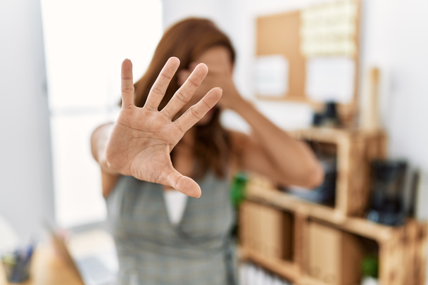 Middle age hispanic woman at the office covering eyes with hands and doing stop gesture with sad and fear expression. embarrassed and negative concept.  - Photo, image
