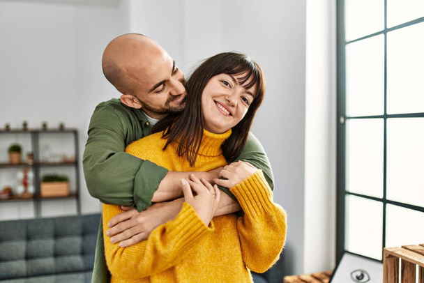 Young hispanic couple smiling happy and hugging standing at home. - Photo, Image