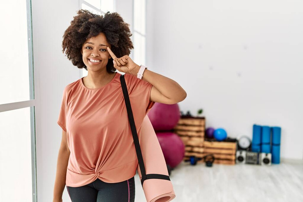 African american woman with afro hair holding yoga mat at pilates room smiling pointing to head with one finger, great idea or thought, good memory  - Valokuva, kuva