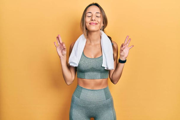 Gyönyörű spanyol nő visel sportruházat és törölköző nyugodt és mosolygós csukott szemmel csinál meditációs gesztus ujjakkal. jóga koncepció.  - Fotó, kép