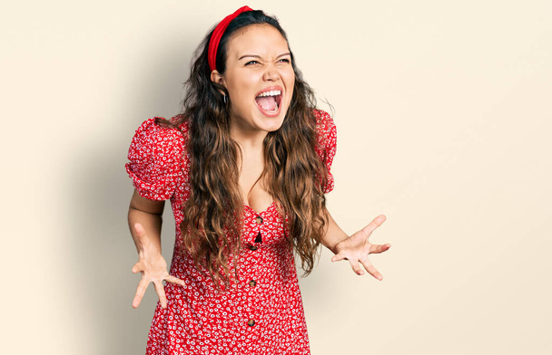 Young hispanic girl wearing casual clothes crazy and mad shouting and yelling with aggressive expression and arms raised. frustration concept.  - Foto, Imagen