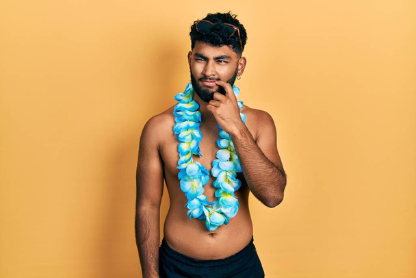 Arab férfi szakállal fürdőruhában és hawaii lei komoly arc gondolkodás kérdés kézzel az állán, gondolkodó zavaros ötlet  - Fotó, kép