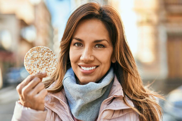 Junge hispanische Frau lächelt glücklich und hält Reiskuchen in der Stadt. - Foto, Bild