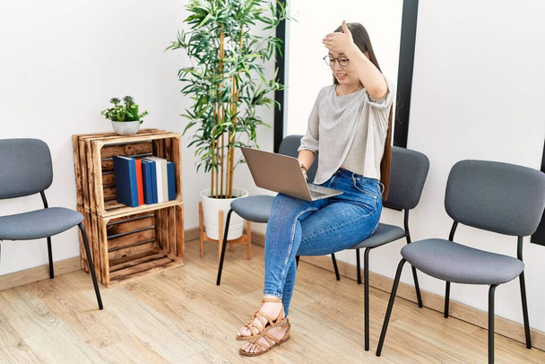 Jeune infirmière asiatique femme assise dans la salle d'attente à l'aide d'un ordinateur portable stressé et frustré avec la main sur la tête, surpris et en colère visage  - Photo, image