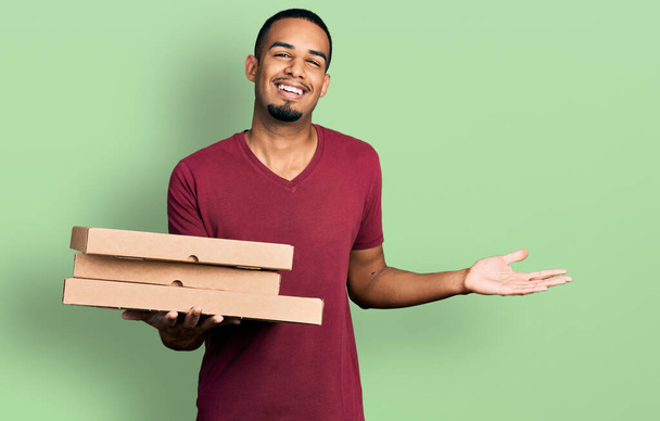 Junger afrikanisch-amerikanischer Mann mit Take-away-Essen feiert Leistung mit glücklichem Lächeln und Siegerausdruck mit erhobener Hand  - Foto, Bild
