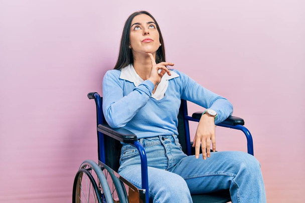 Bella donna con gli occhi azzurri seduta sulla sedia a rotelle pensando concentrato sul dubbio con il dito sul mento e guardando verso l'alto chiedendo  - Foto, immagini