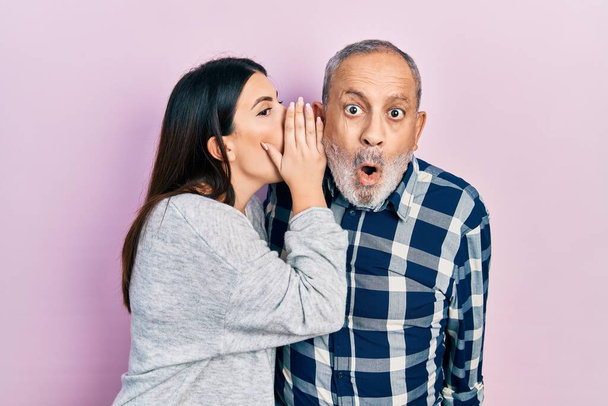 El padre y la hija hispanos llevando ropa casual mano a boca contando rumores secretos, susurrando conversaciones maliciosas  - Foto, Imagen