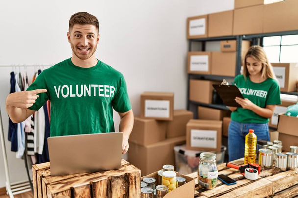 Young man and woman wearing volunteer t shirt at donations stand pointing finger to one self smiling happy and proud  - Foto, Imagen