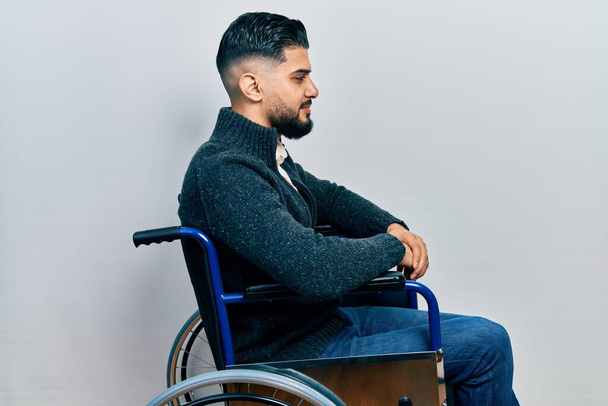 Красивий чоловік з бородою сидить на інвалідному візку, дивлячись в бік, розслабляє профільну позу з природним обличчям з впевненою посмішкою
.  - Фото, зображення
