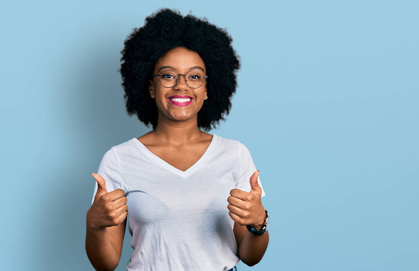 Fiatal afro-amerikai nő alkalmi fehér pólót visel siker jel csinál pozitív gesztus kézzel, hüvelykujj fel mosolyogva és boldogan. vidám kifejezés és győztes gesztus.  - Fotó, kép