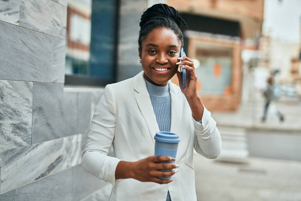 Mladá africká americká obchodnice mluví na smartphone a pití kávy ve městě. - Fotografie, Obrázek
