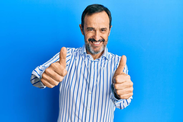 Hombre hispano de mediana edad vistiendo ropa casual aprobando hacer gesto positivo con la mano, pulgares arriba sonriendo y feliz por el éxito. gesto ganador.  - Foto, imagen